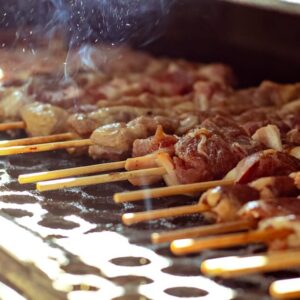 Delicious meat skewers grilling on an open barbecue with smoke rising.