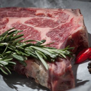 Close-up of a raw steak garnished with rosemary and chilies, ideal for cooking concepts.