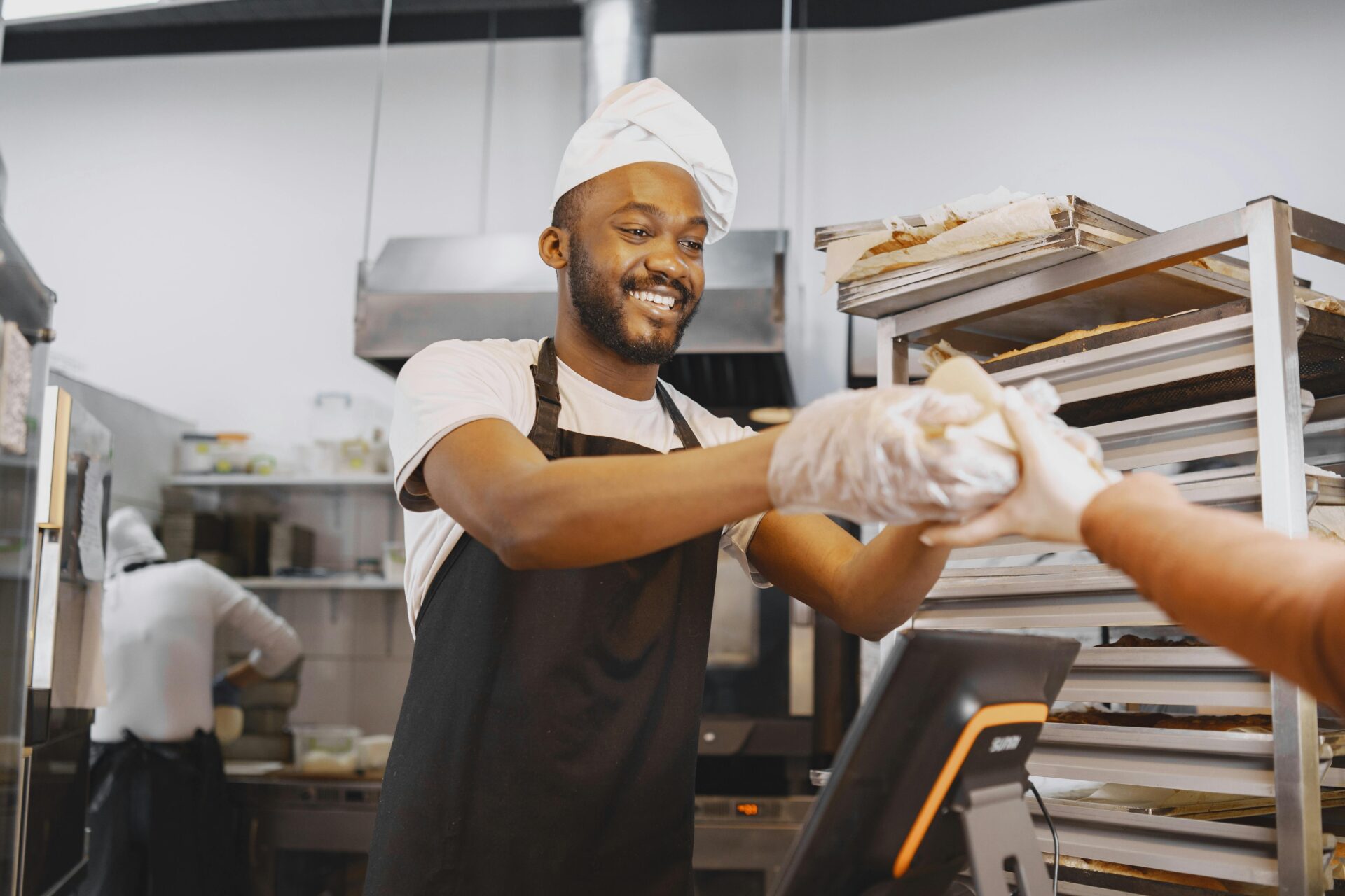 A cheerful baker in a kitchen giving fresh bread to a customer. Perfect for culinary or bakery-themed content.