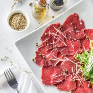 Delicious beef carpaccio with capers, olive oil, and fresh toppings on a white plate.